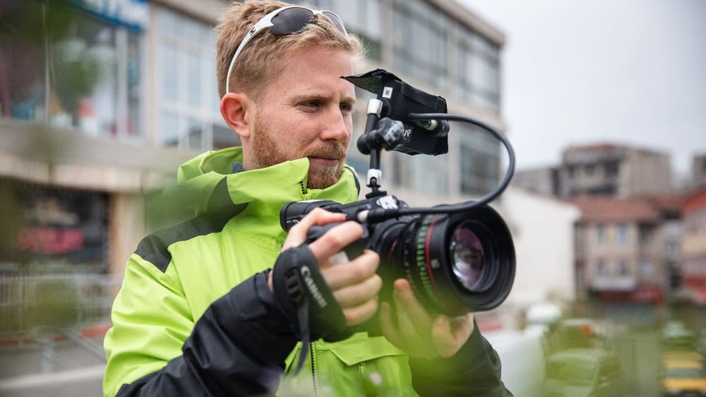 A filmmaker in a bright jacket filming with a handheld camera