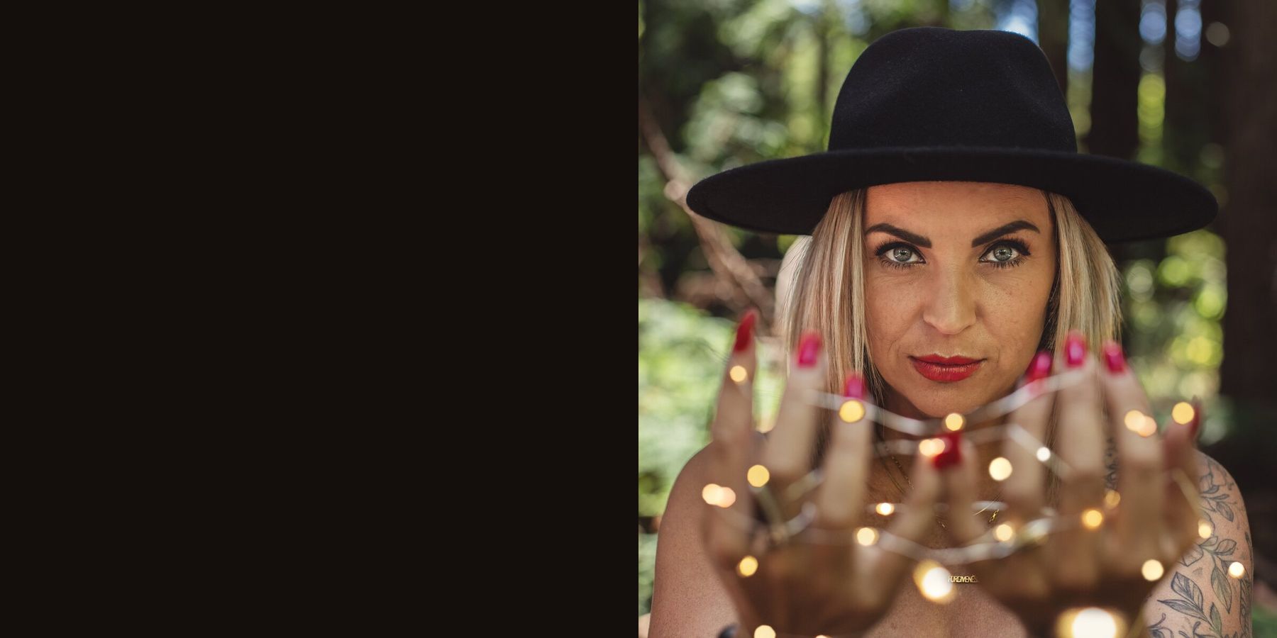 Victoria Bond in a black wide brim hat, holding fairy lights in her cupped hands in the forest