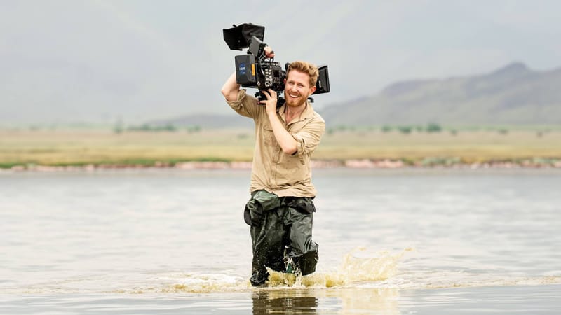 Sebastian wading through a lake with a camera on his shoulder