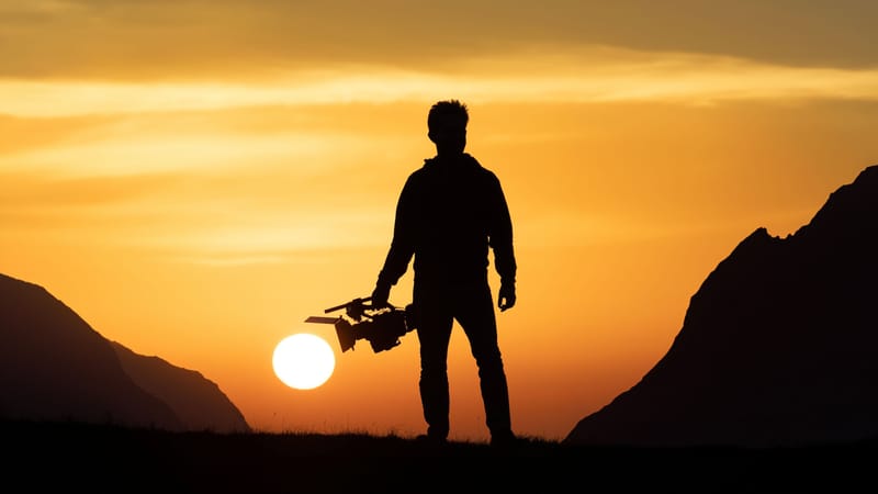 Silhouette of a filmmaker holding a camera at sunset
