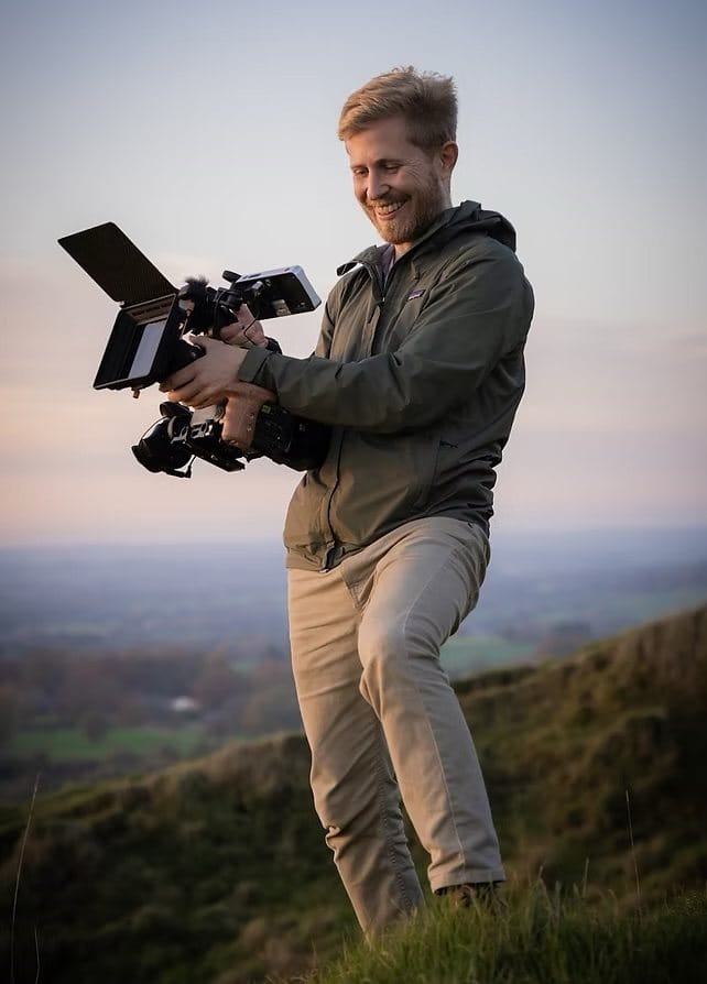 Sebastian Solberg smiling as he films on a hillside at dusk