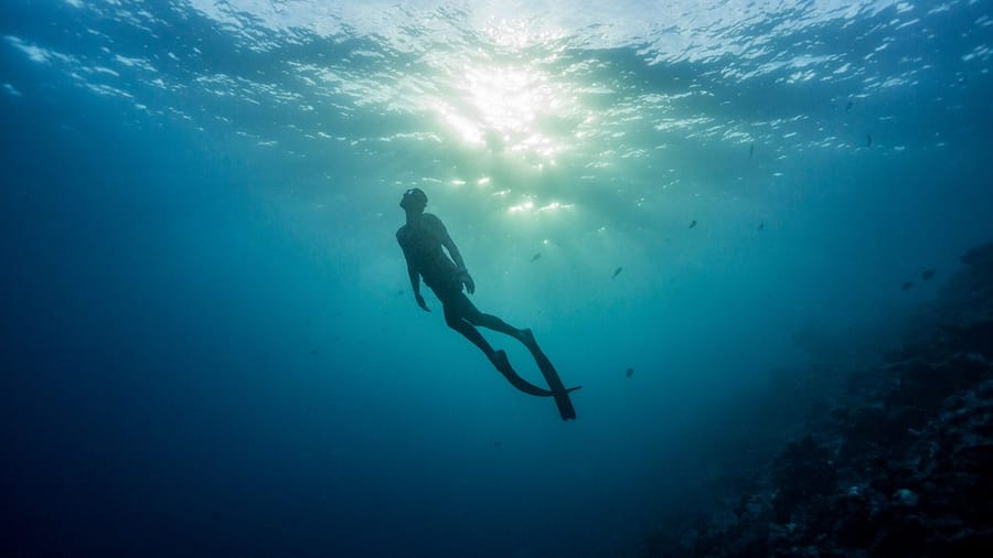 A freediver swimming up towards the light