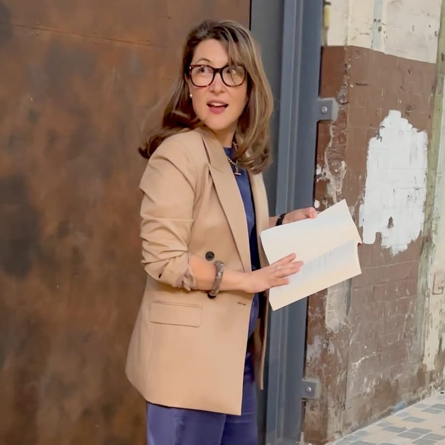 Sonya Choi La Rosa in a camel blazer over navy, notes in hand, turning to speak