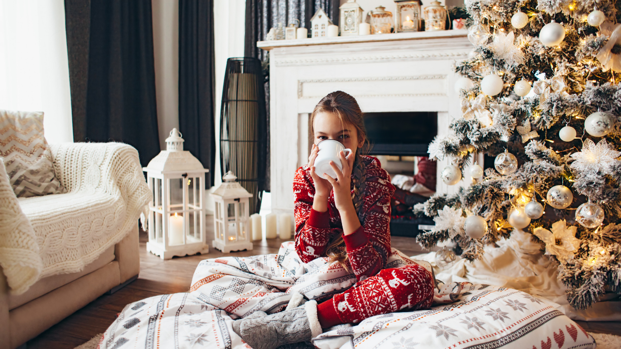 Woman in christmas pajamas sipping from a mug in front of a christmas tree and decorations holiday selling tips can help you enjoy the holidays