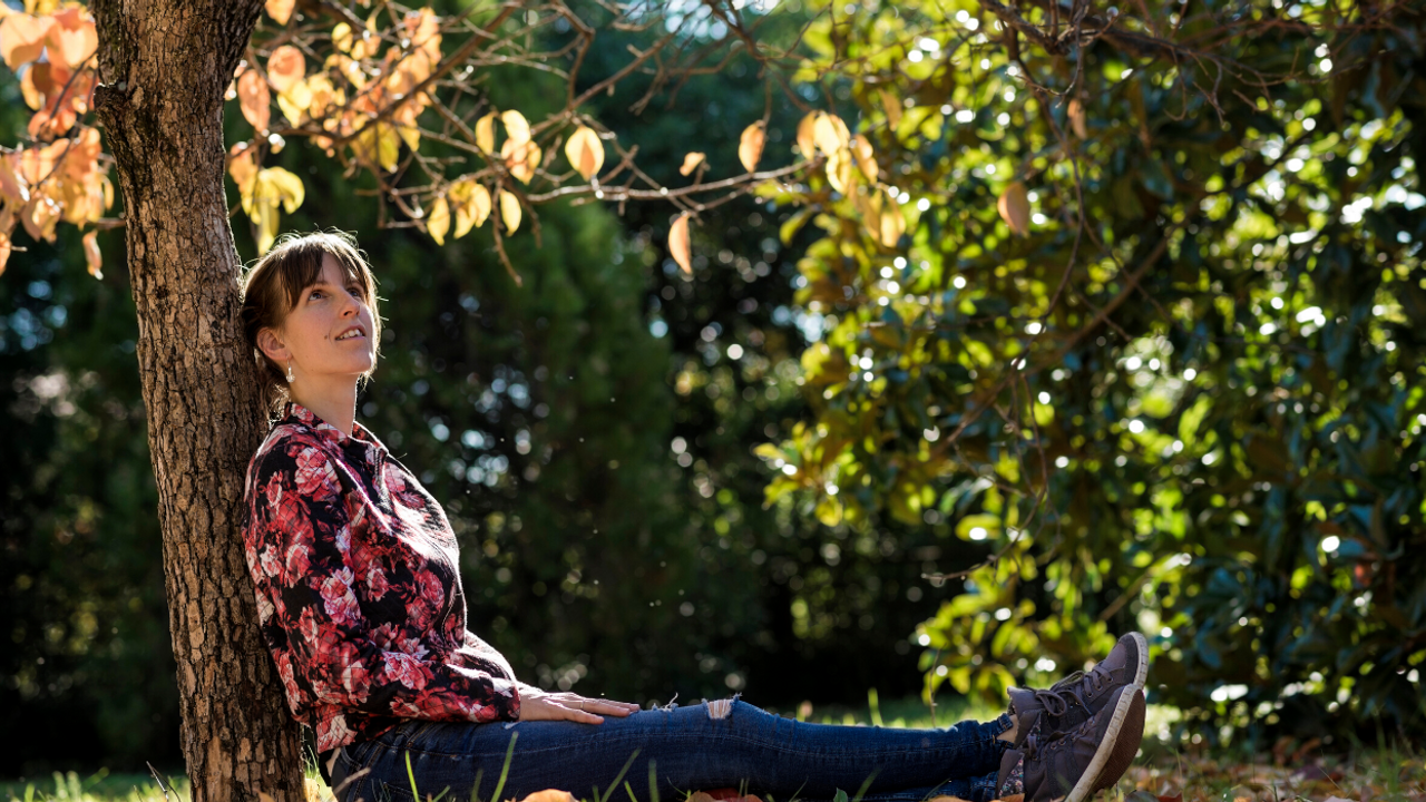 Woman sitting under a tree looking up at the leaves