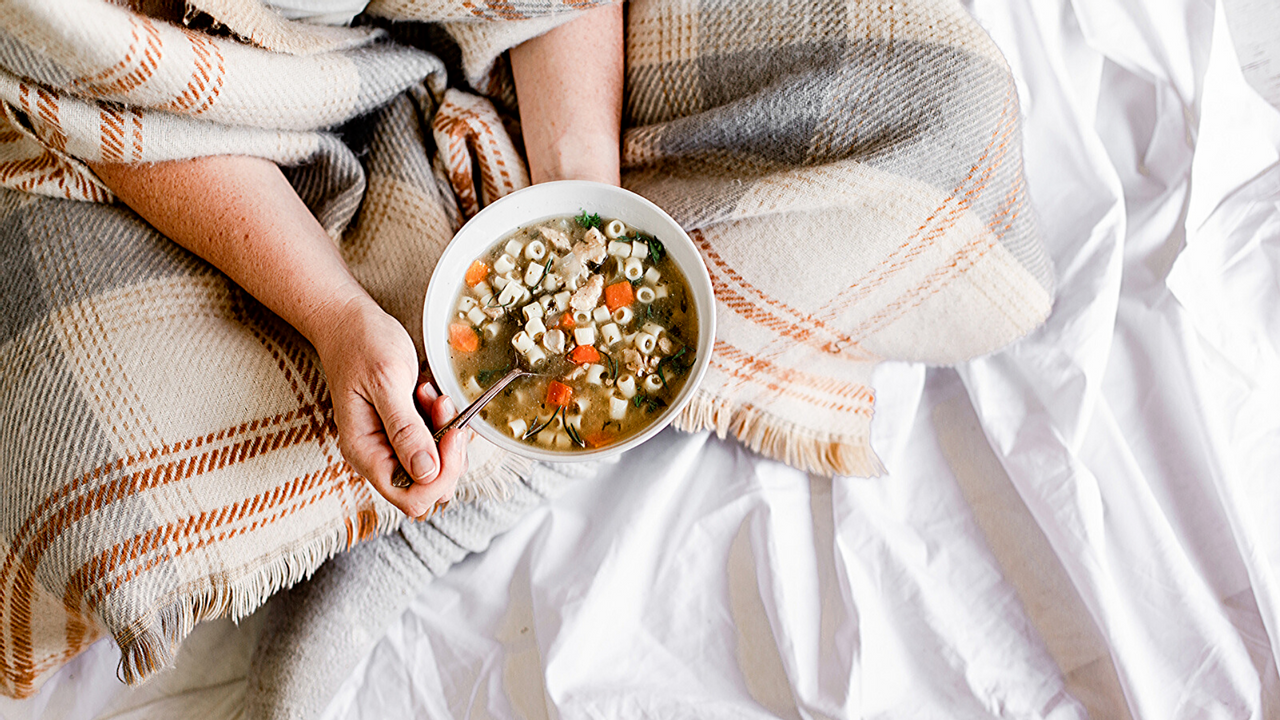 a person wrapped in a blanket eating chicken soup
