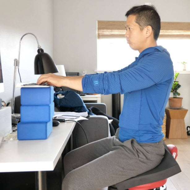 Matt Hsu, the founder of Upright Health, sits at his computer with his hands too high, demonstrating bad sitting posture. 