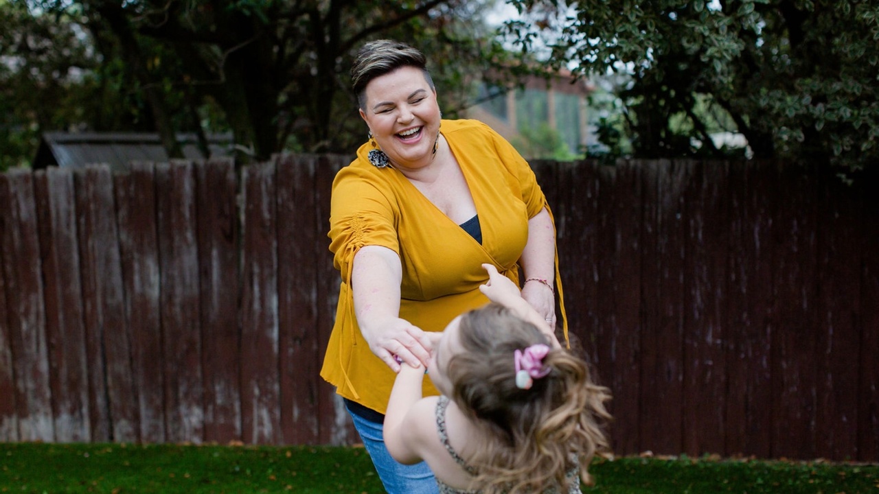 Photo of a woman and child playing and laughing together, holding hands in a backyard.