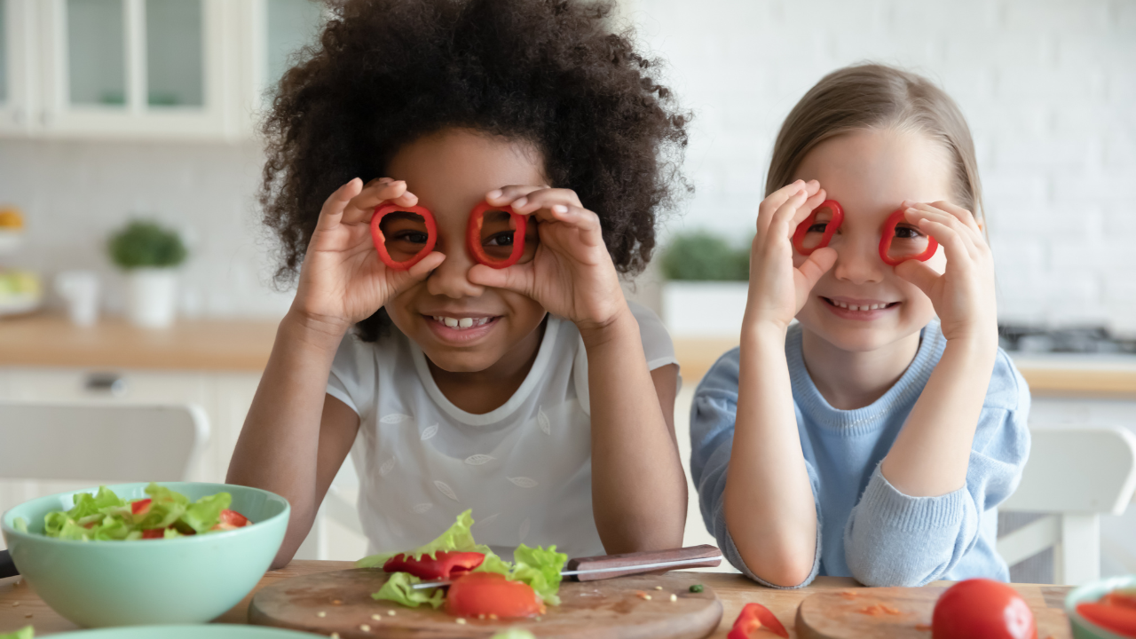 two kids playing with bell pepper rings and wearing them like glasses while making a salad