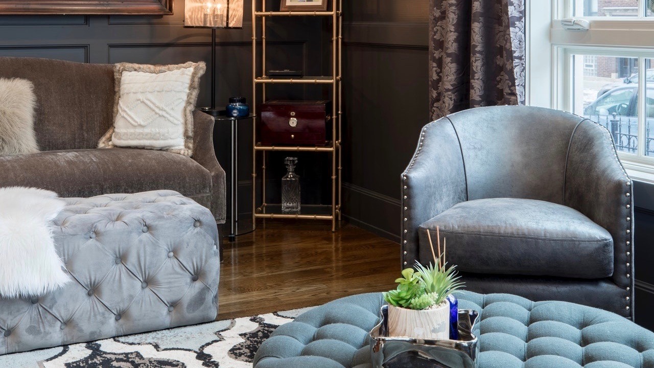 Styled room in home. Colors are gray, sea foam, charcoal, cream, black, and brass. Fabric ottomans are tufted velvet and nailhead trimmed leather furniture.