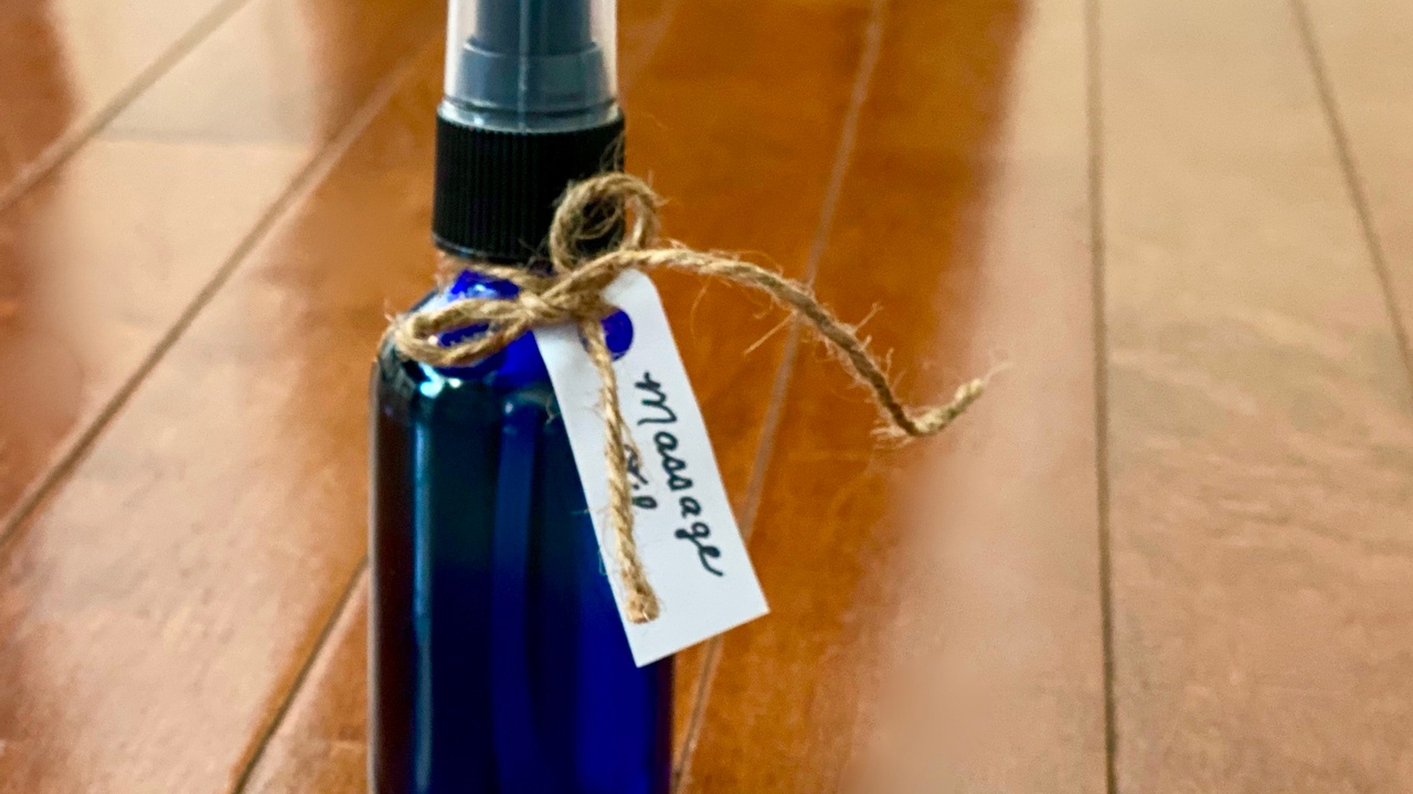 Cobalt blue spray bottle labeled massage oil sitting on wood floor.