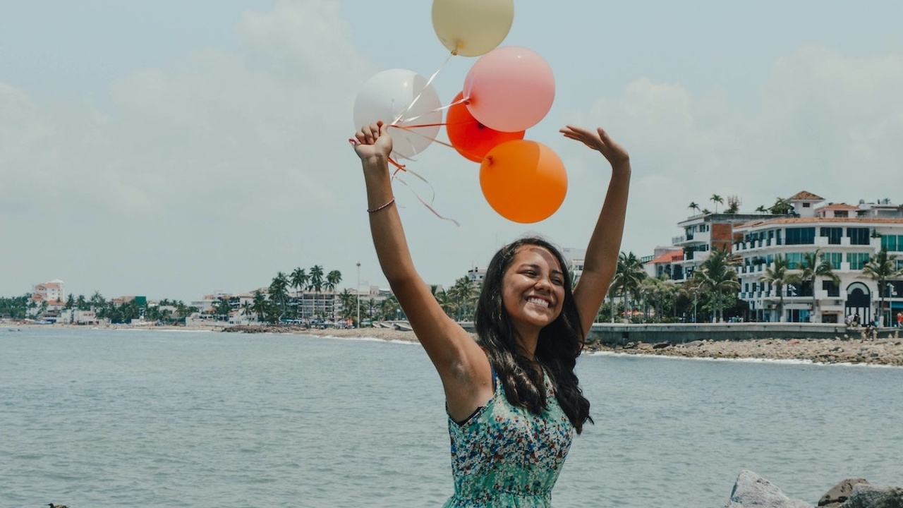 young woman sitting on shore holding balloons