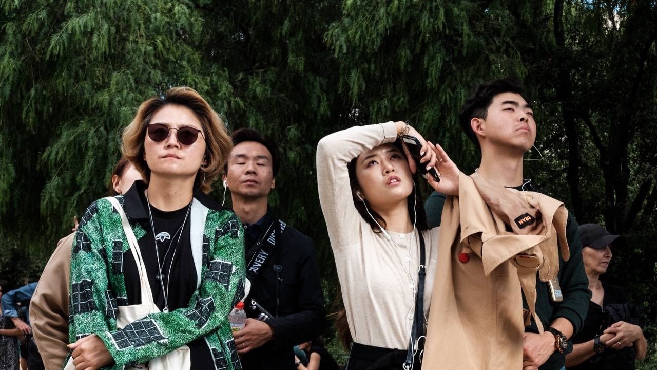 Street photography of group of people some with eyes closed against a greenery backdrop