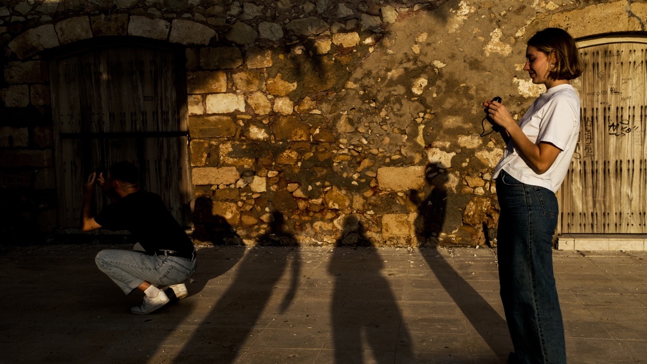 Street photography of man crouching, a row of shadows and a woman holding a camera