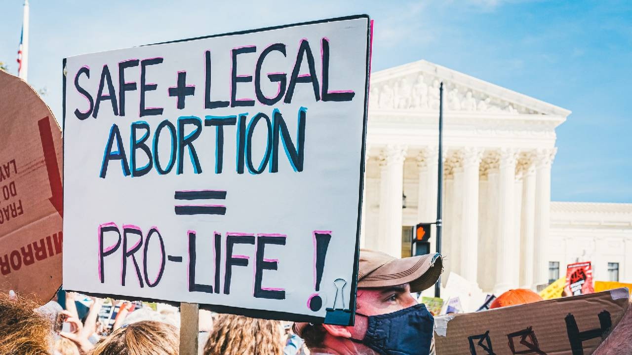 protesters march with a sign that reads safe + legal abortions = pro-life!