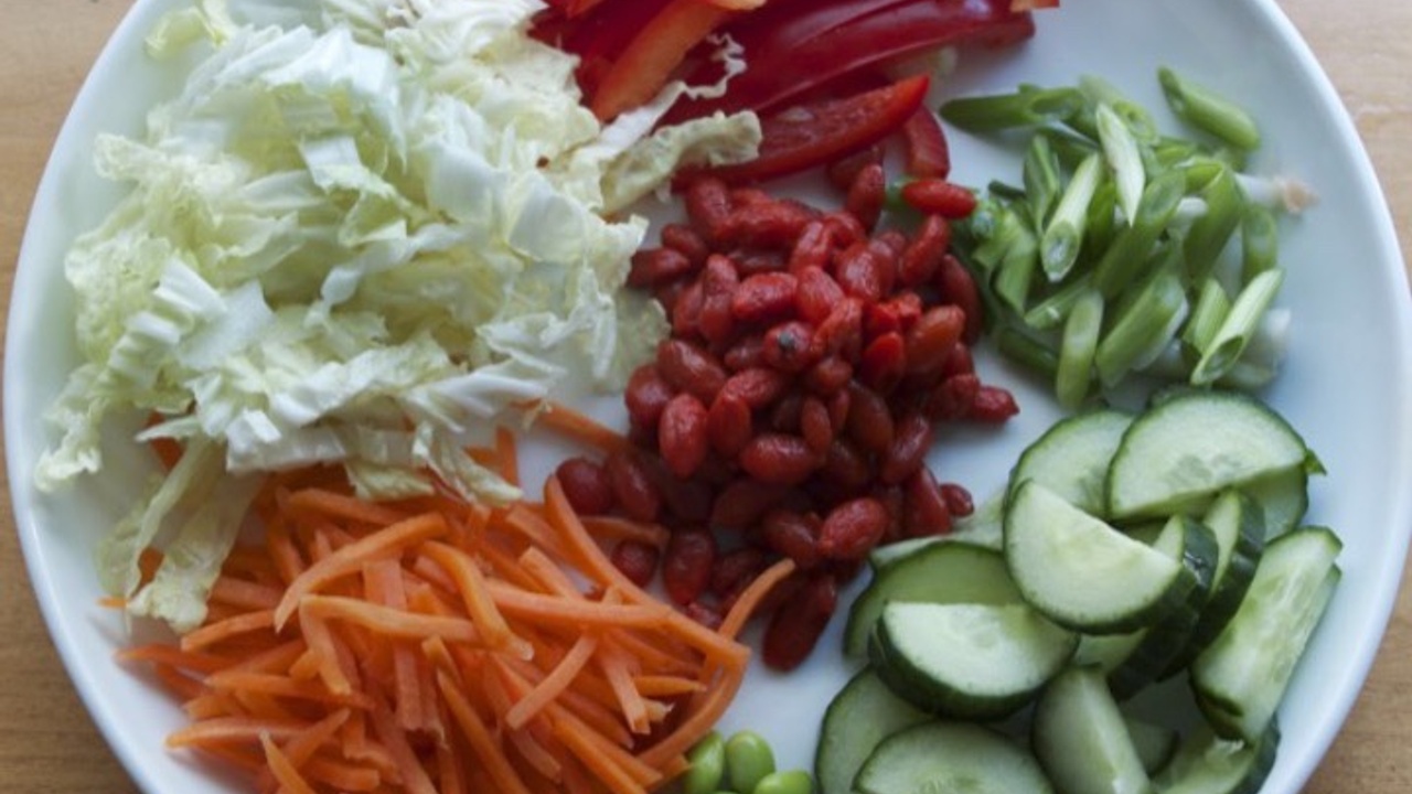 plate with shredded cabbage, cut up cucumber, sliced red pepper, shredded carrots, sliced green onion and goji berries