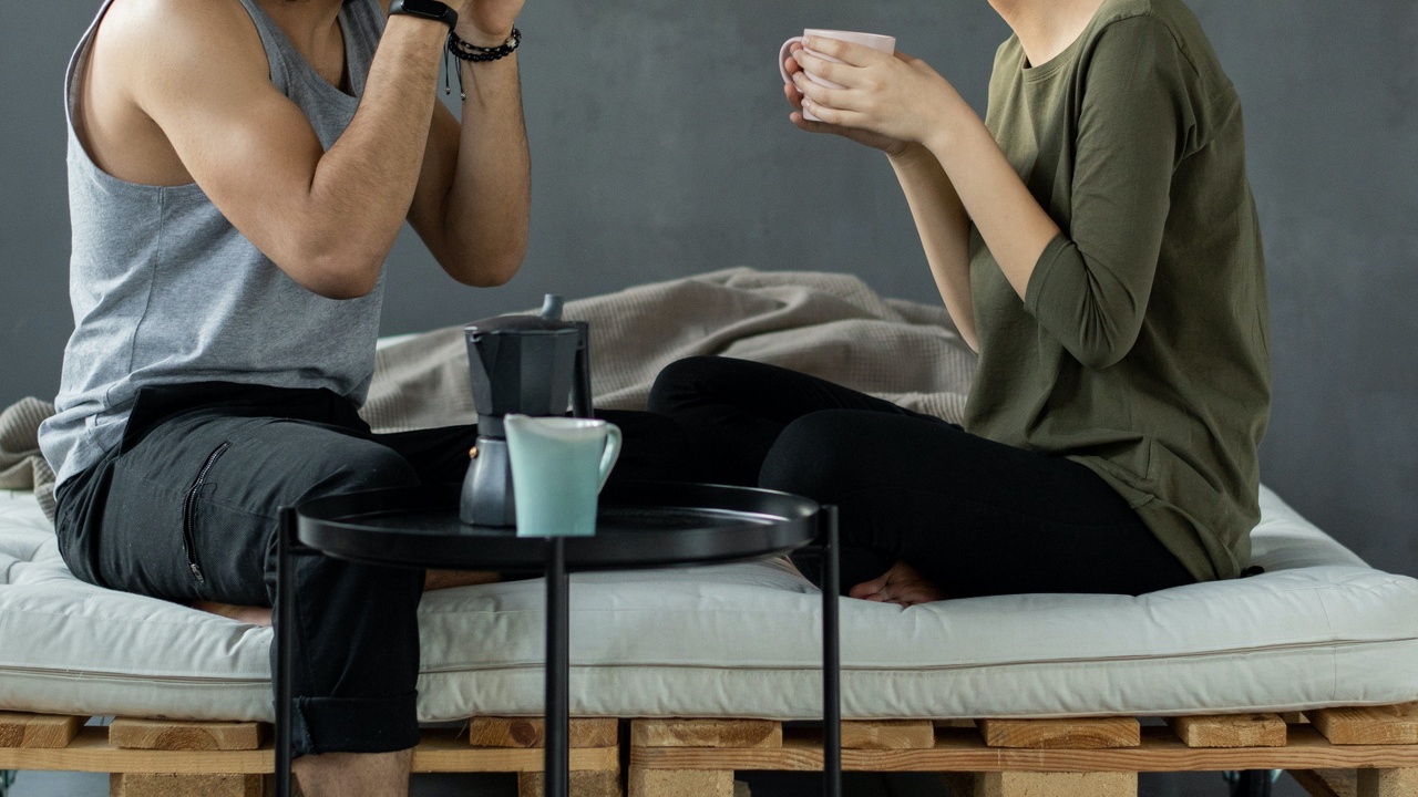 Couple seated on a platform bed sipping tea and talking.