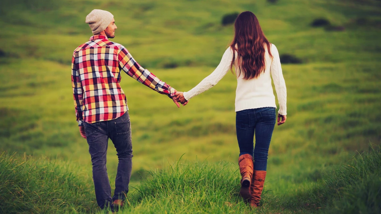 Woman and Man holding hands and walking in a grassy area