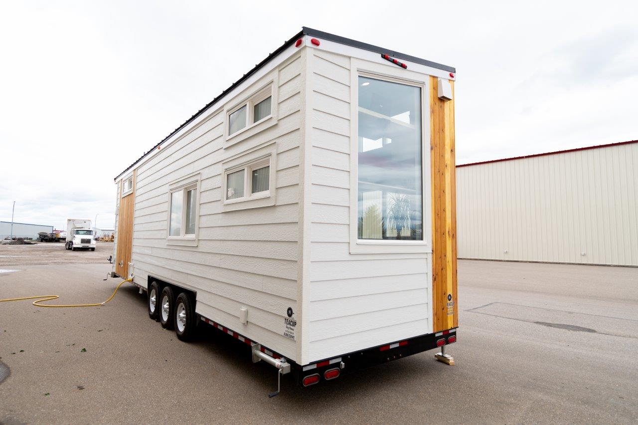 The exterior of a tiny home showing siding, tires, jacks and chassis.