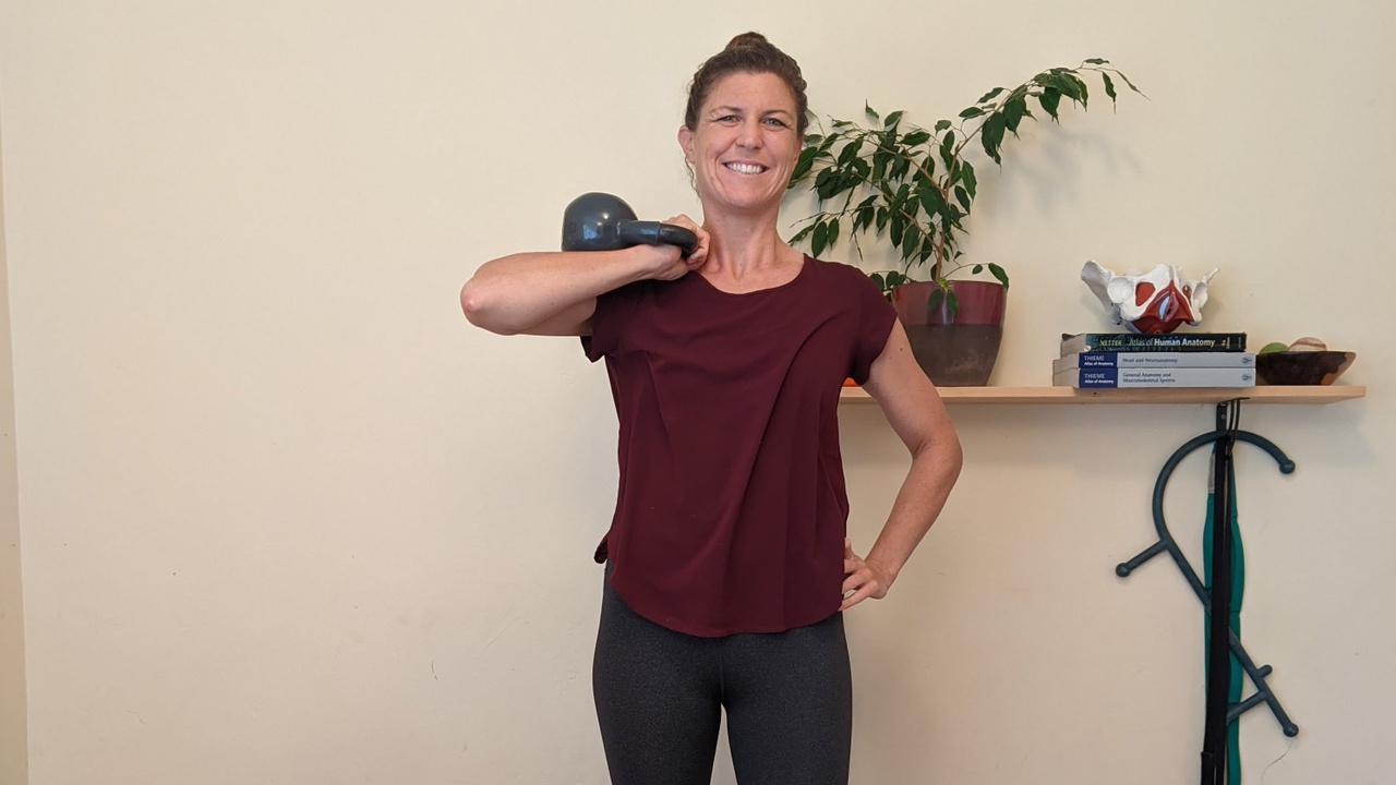 A woman smiles as she holds a kettlebell in front rack position.