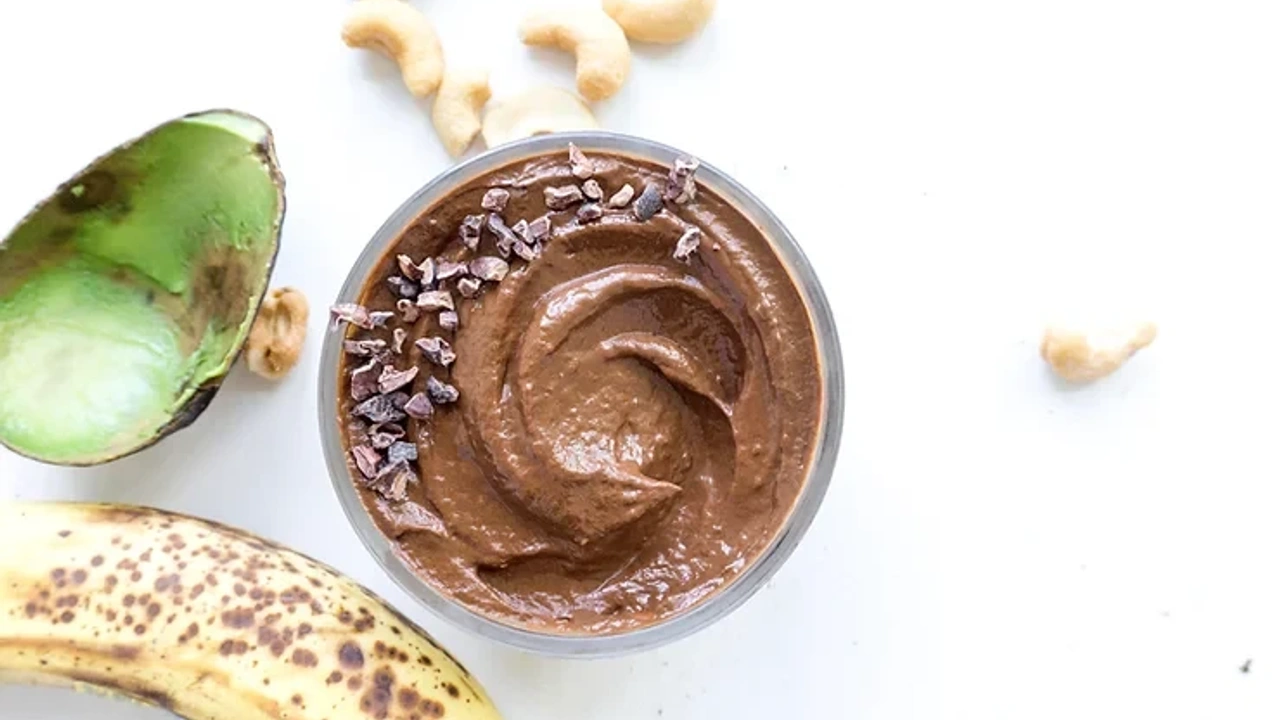 A bowl of chocolate avocado pudding with cacao nibs, nuts, and a banana