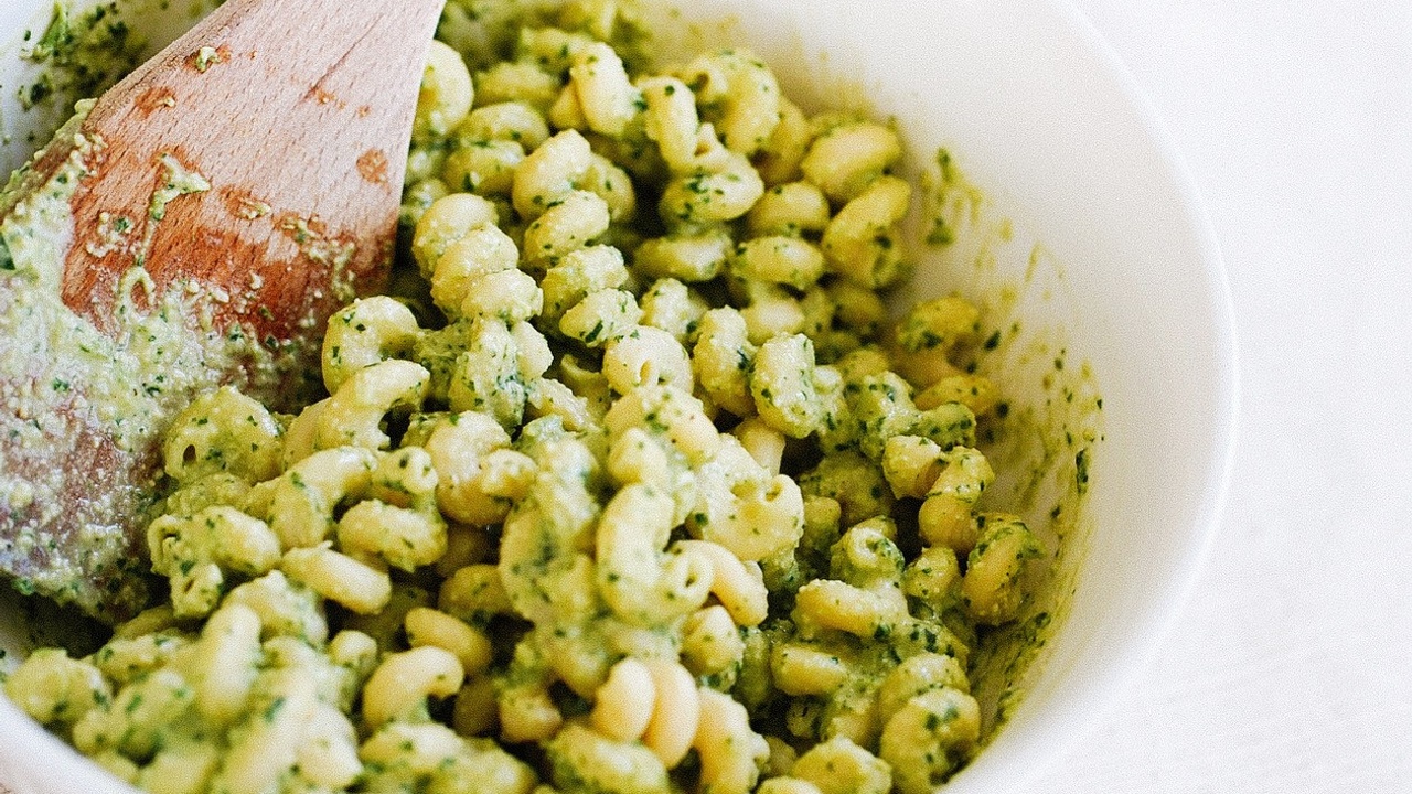 Spiral pesto pasta in a white bowl with a wooden spoon