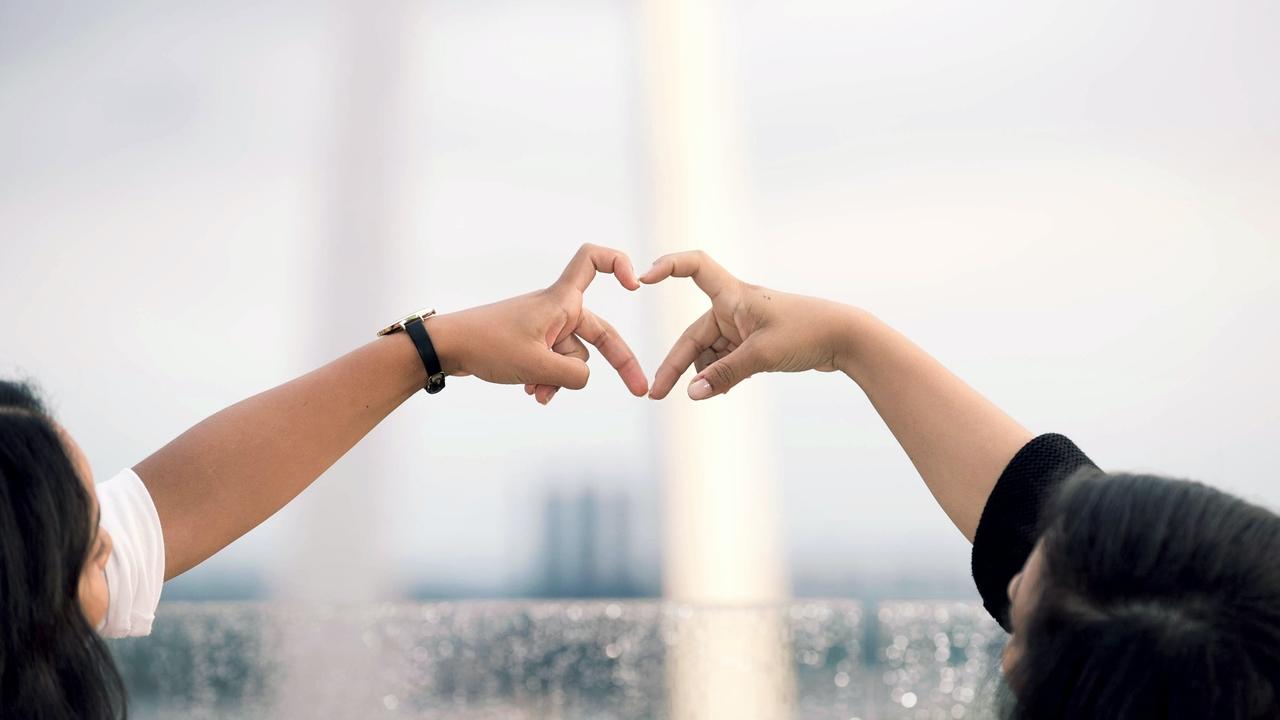 Two people creating a heart symbol with fingers in front of St. Louis Arch