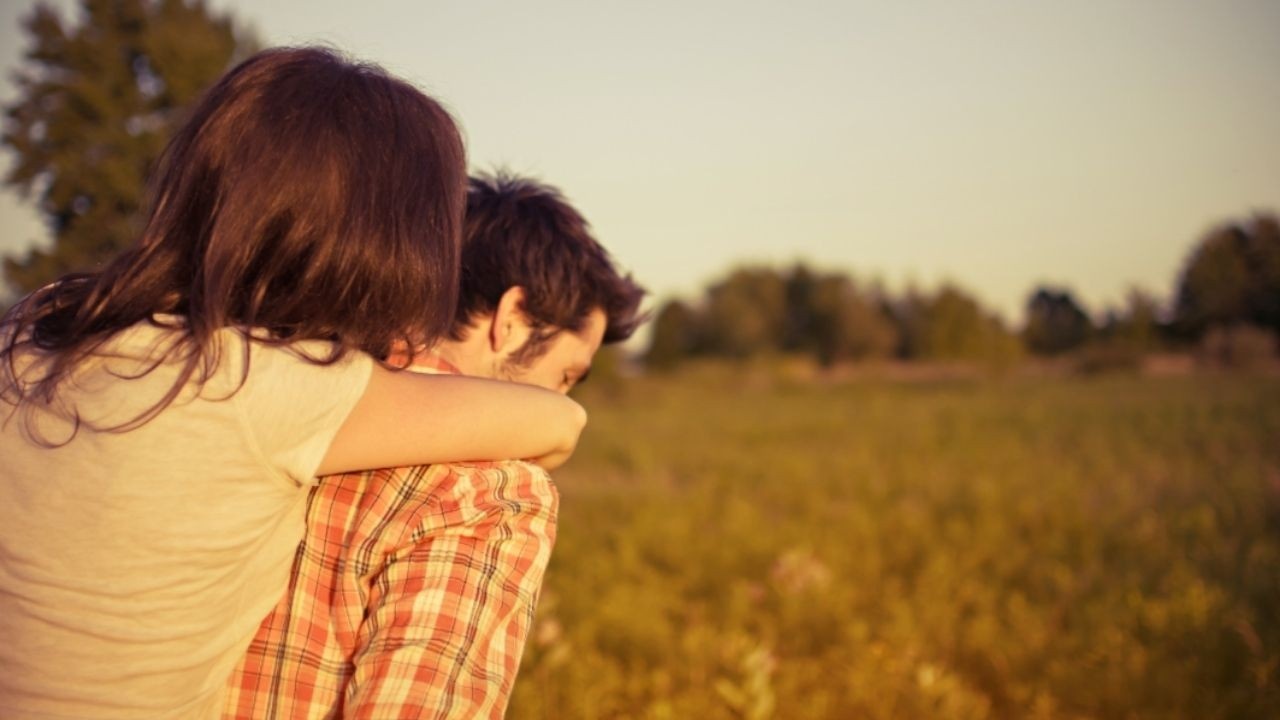 A woman is lovingly carried on the back of a man as they walk through a field