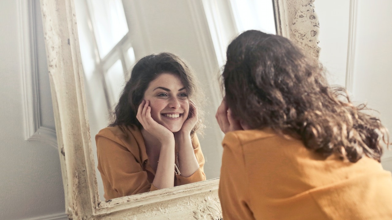  A smiling woman looks at a mirror reflection.