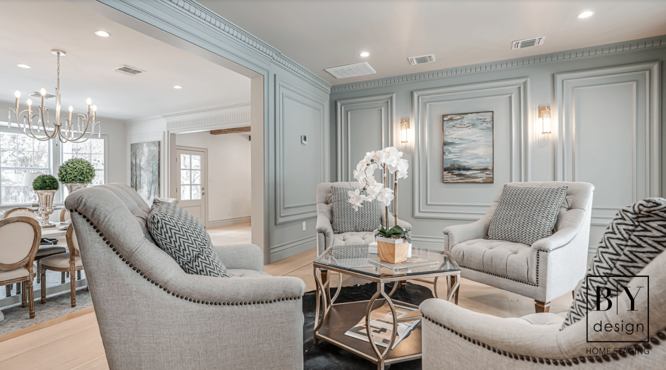 Blue green wall with trim on it all painted the same colo with bulky off white chairs around a glass coffee table.