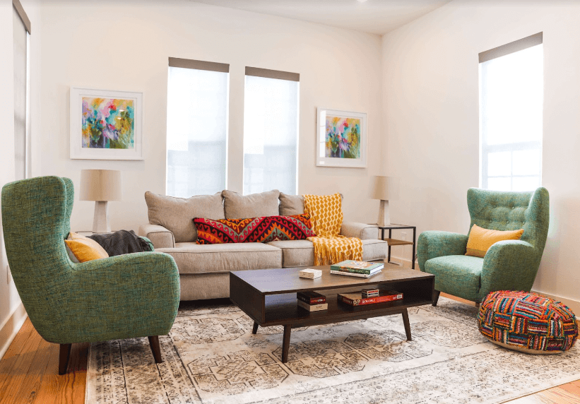 Living room with gray couch and and green chairs with patterned pillows and blankets.