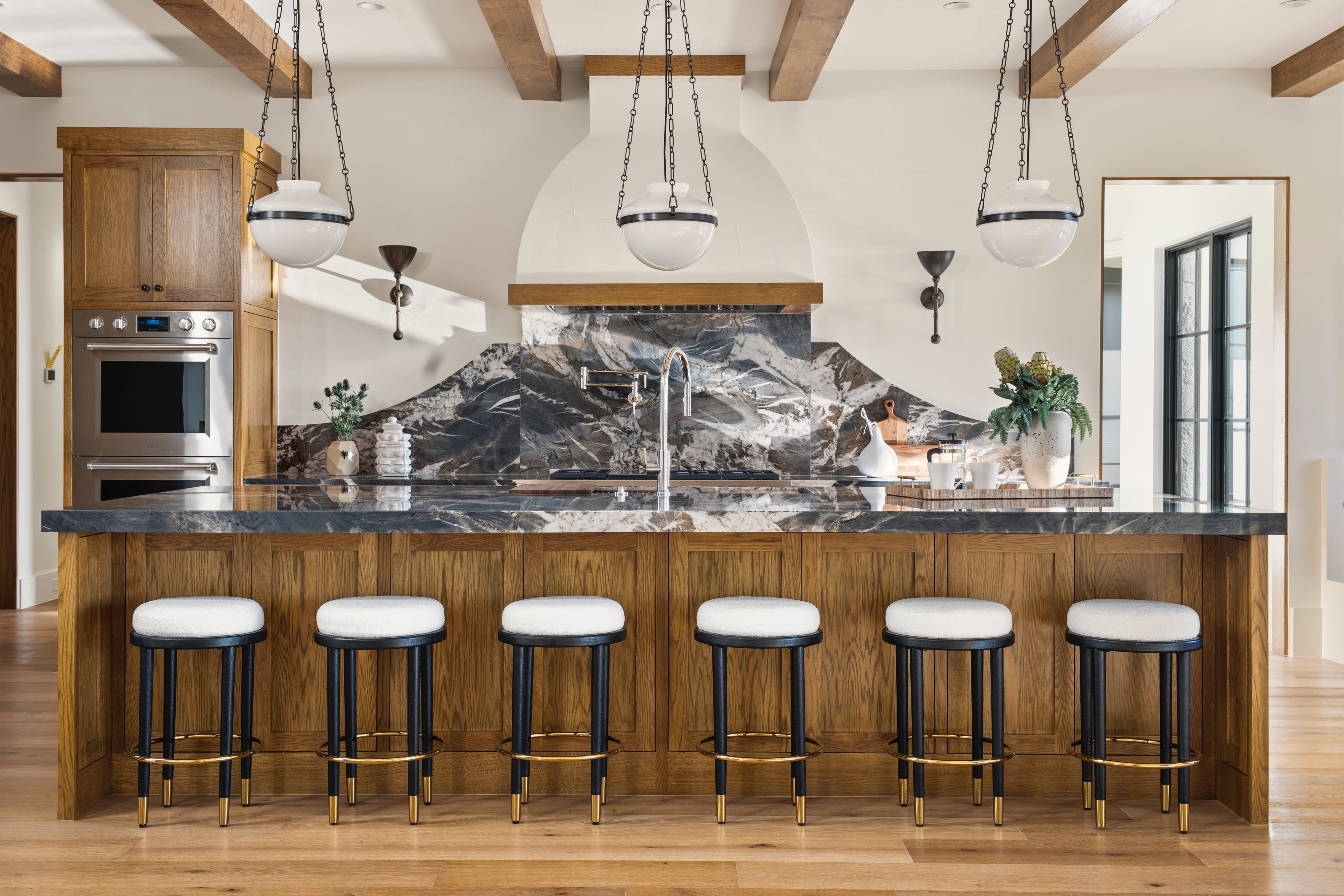 Large kitchen island with dark marble counter, wood cabinets, and six barstools.