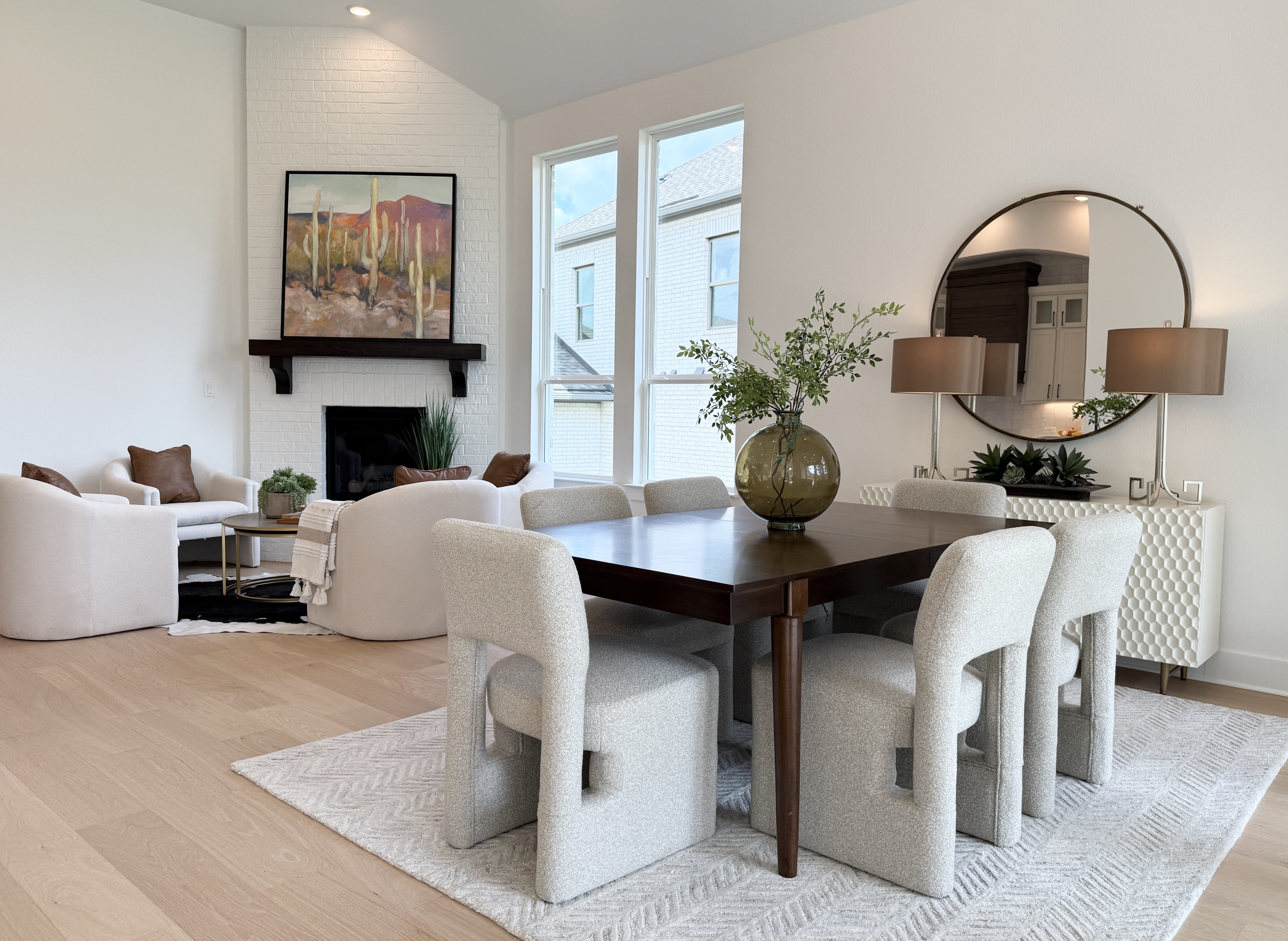 Modern open-concept dining and living area with textured gray chairs, a dark wood table, and a white brick fireplace.