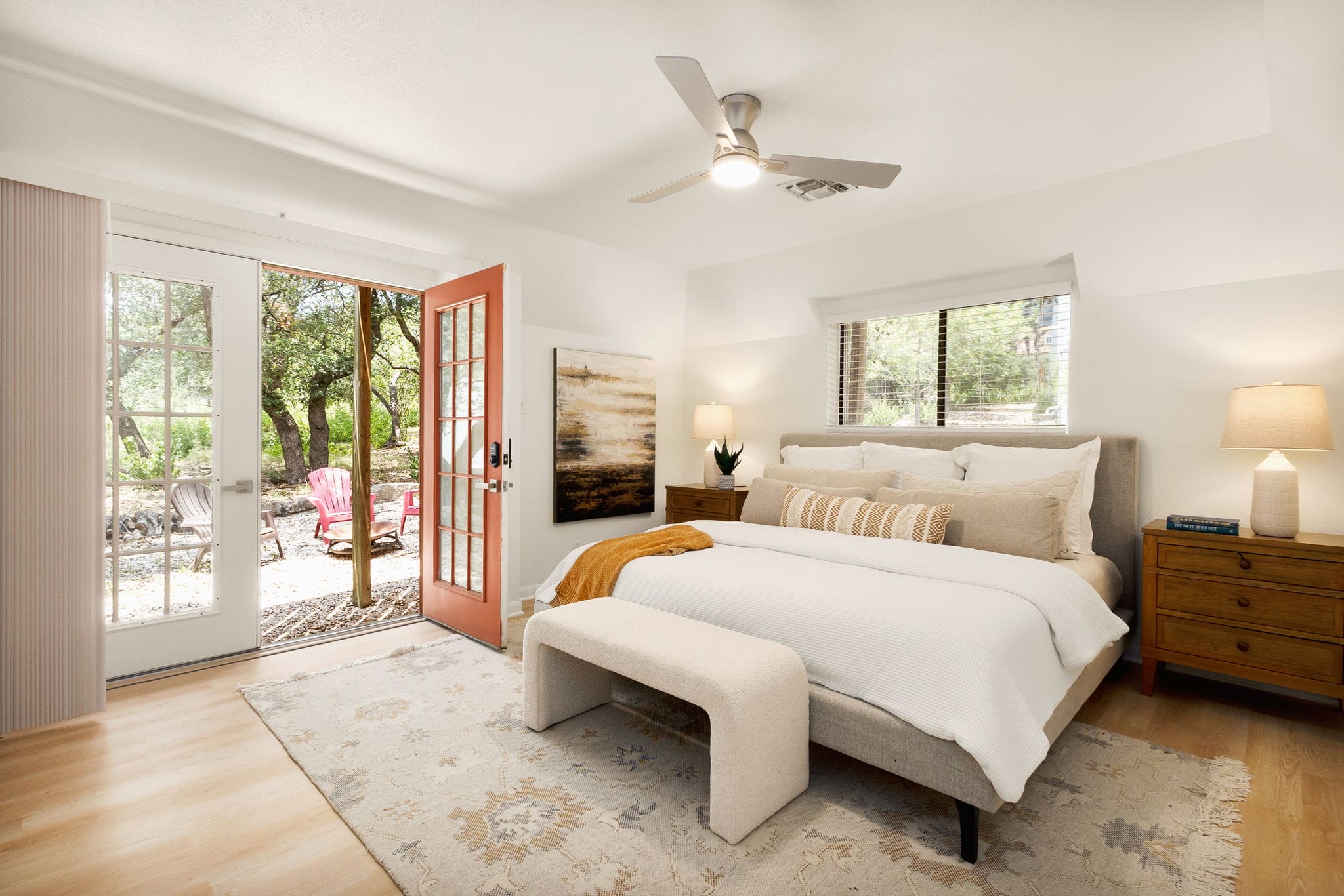 Primary suite with white bedding and open French doors leading to a wooded patio.