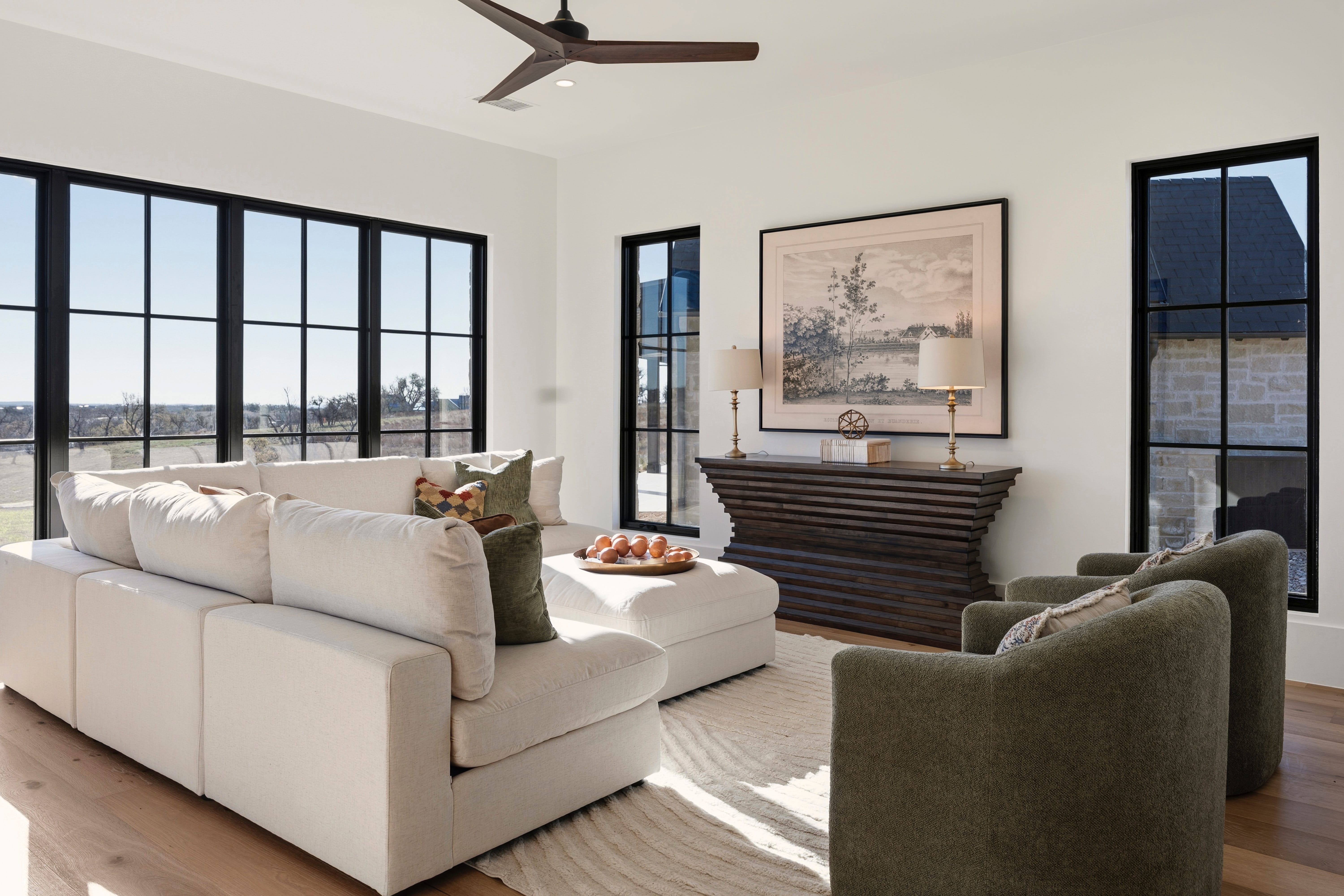 Seating area with a cream sectional sofa, green armchairs, and large black-frame windows.