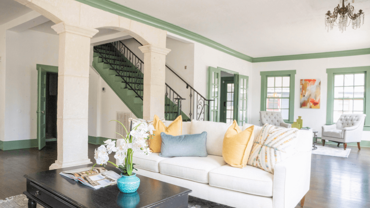 Staged living room using off white couch and yellow pillows with white walls and green trim.