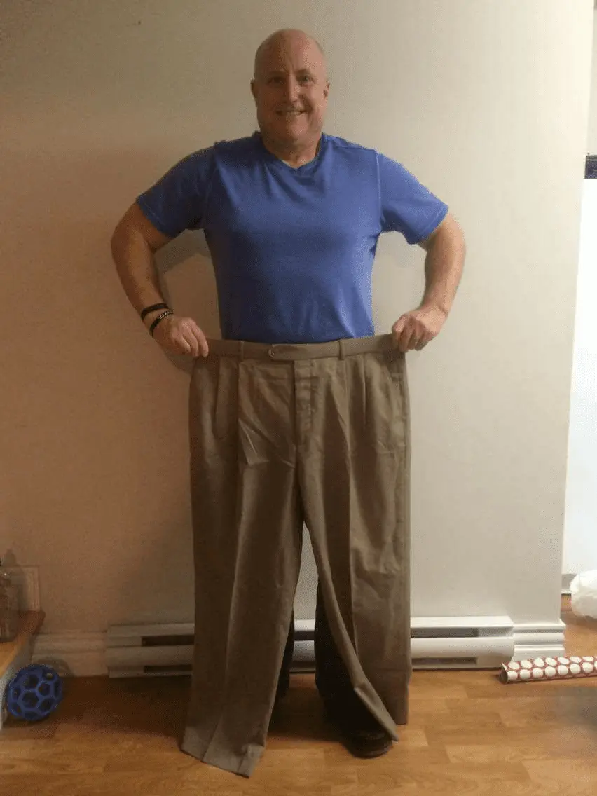 Doug Collins showcasing his weight loss success by holding up his old, now oversized pants after losing 100 pounds.