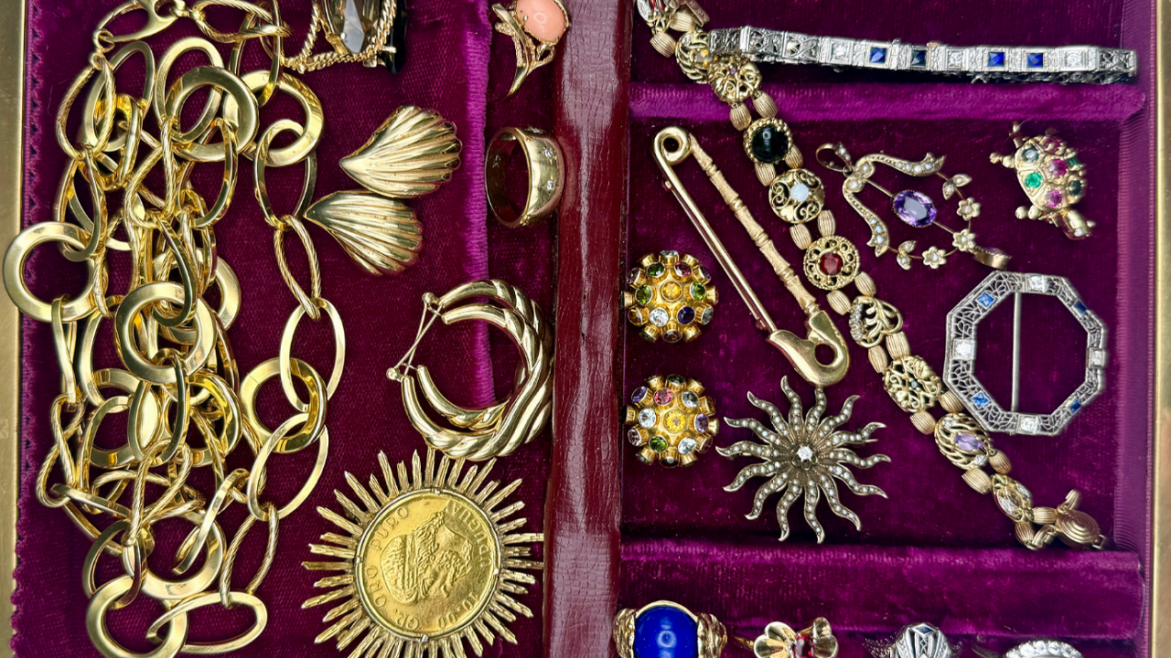 Vintage jewelry collection displayed in a velvet tray, including gold chains, brooches, gemstone rings, Art Deco bracelets, and colorful statement pieces.