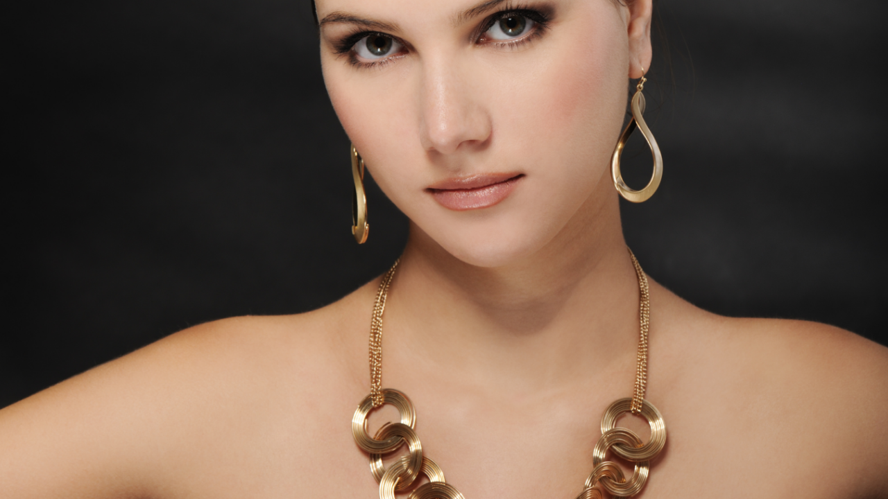 Confident woman wearing bold gold statement necklace and earrings against a dark background, symbolizing goddess strength and elegance.