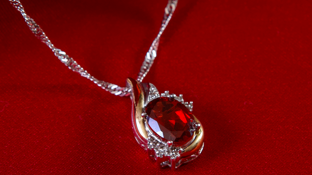 Vintage garnet pendant with deep red gemstone set in silver and gold with diamond accents on a red background.