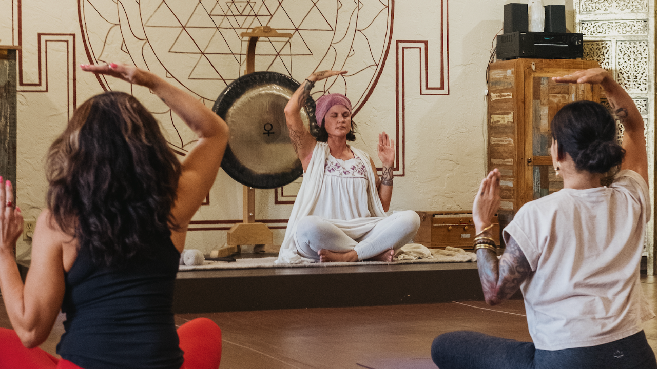 Yogalution Movement Yoga Class with a Gong and Sri Yantra painted on the wall, with three ladies practicing yoga.