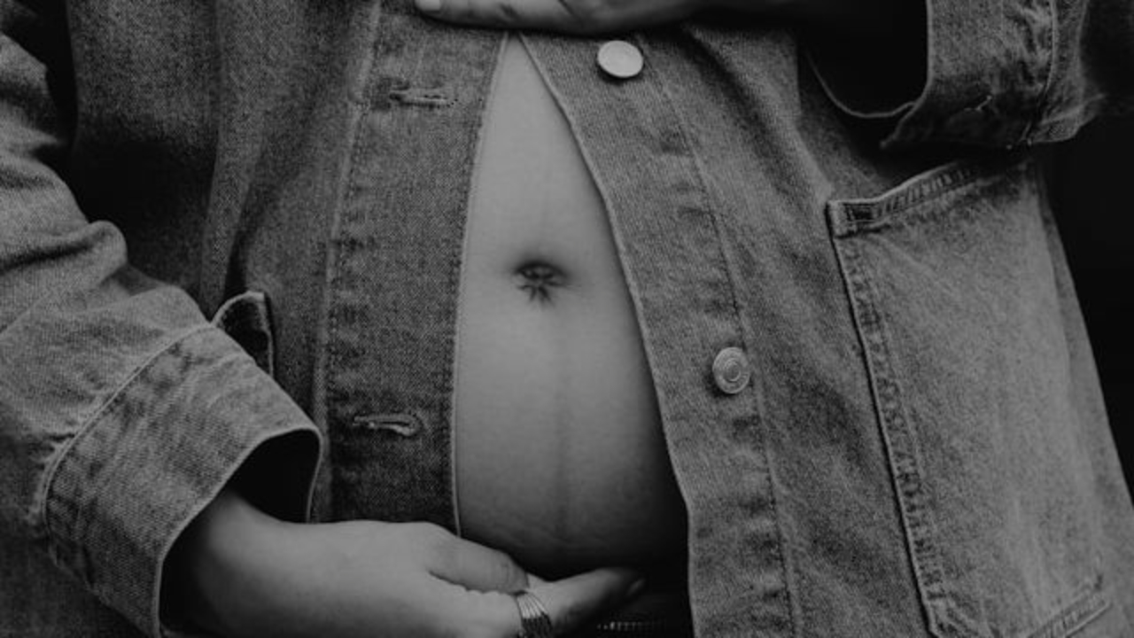 a black and white image of a woman holding her pregnant belly she is wearing a denim jacket.