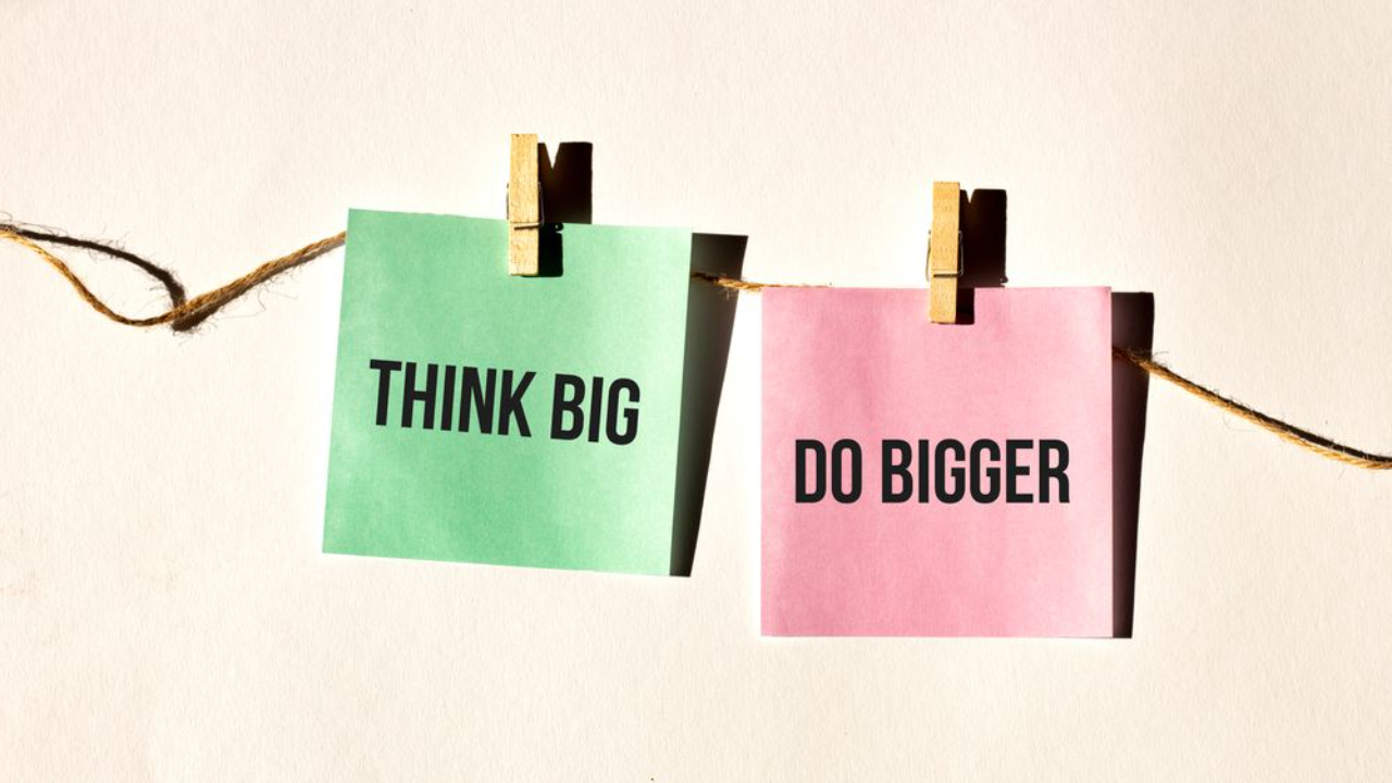 Two pastel sticky notes clipped to a string reading “Think Big” and “Do Bigger.”