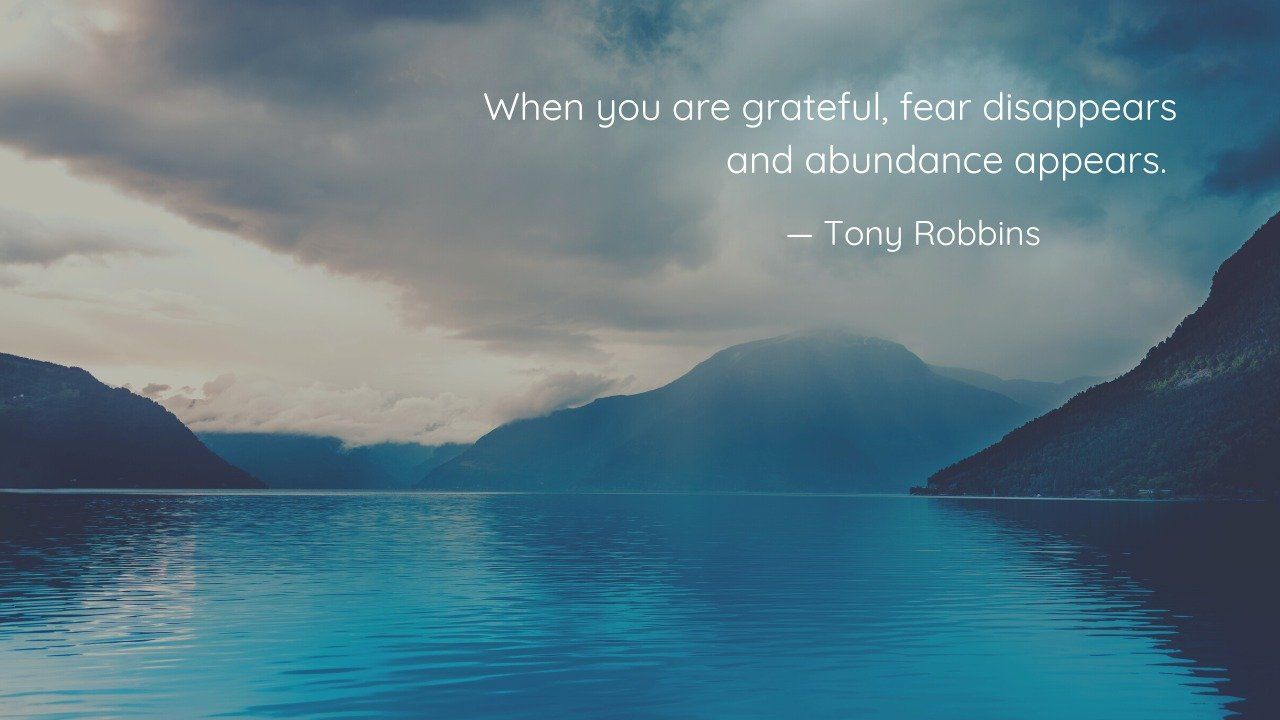 Serene lake surrounded by mountains under a cloudy sky with Tony Robbins' quote: 'When you are grateful, fear disappears and abundance appears.