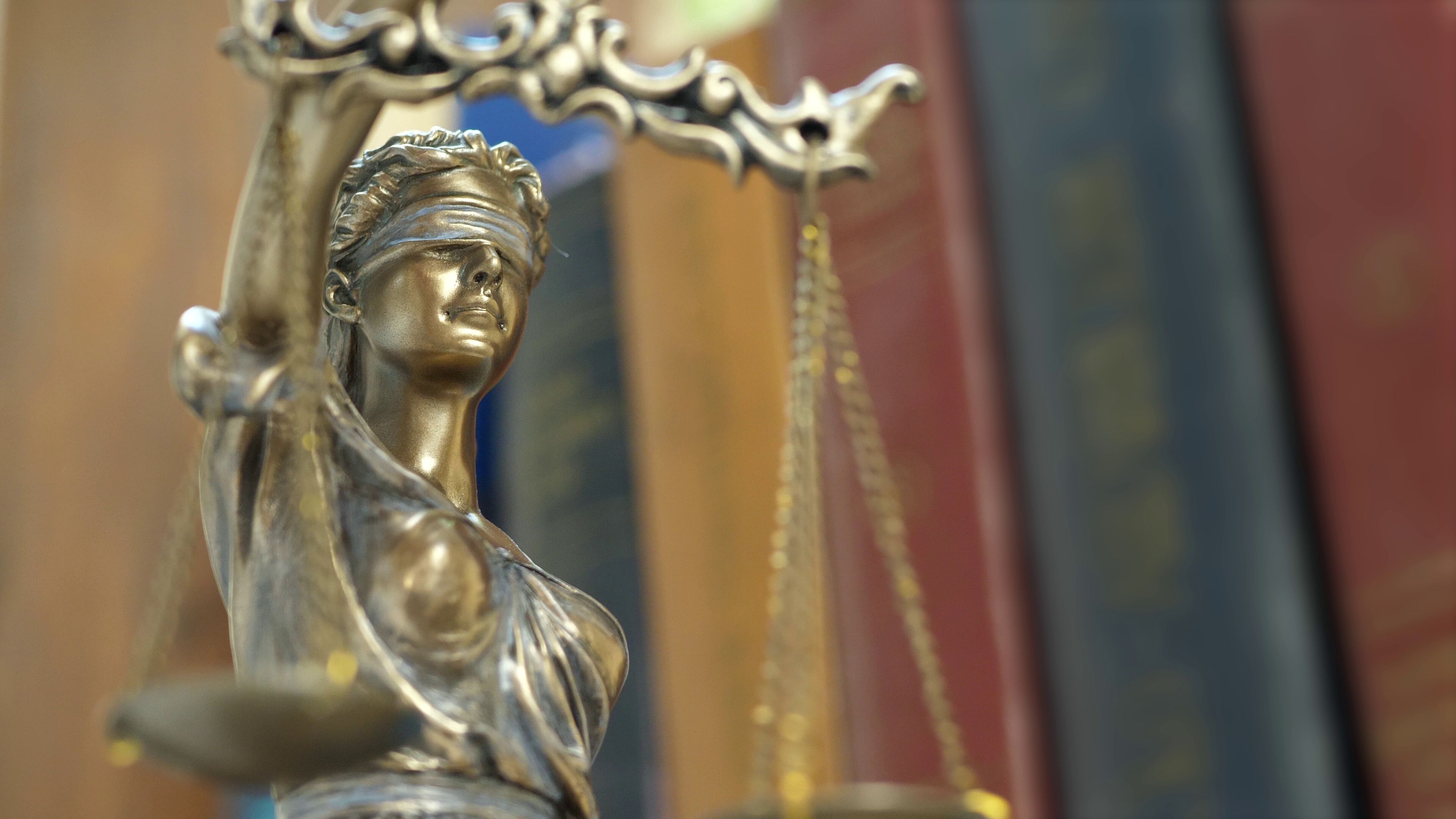 A statue of the scales of justice in front of old books.