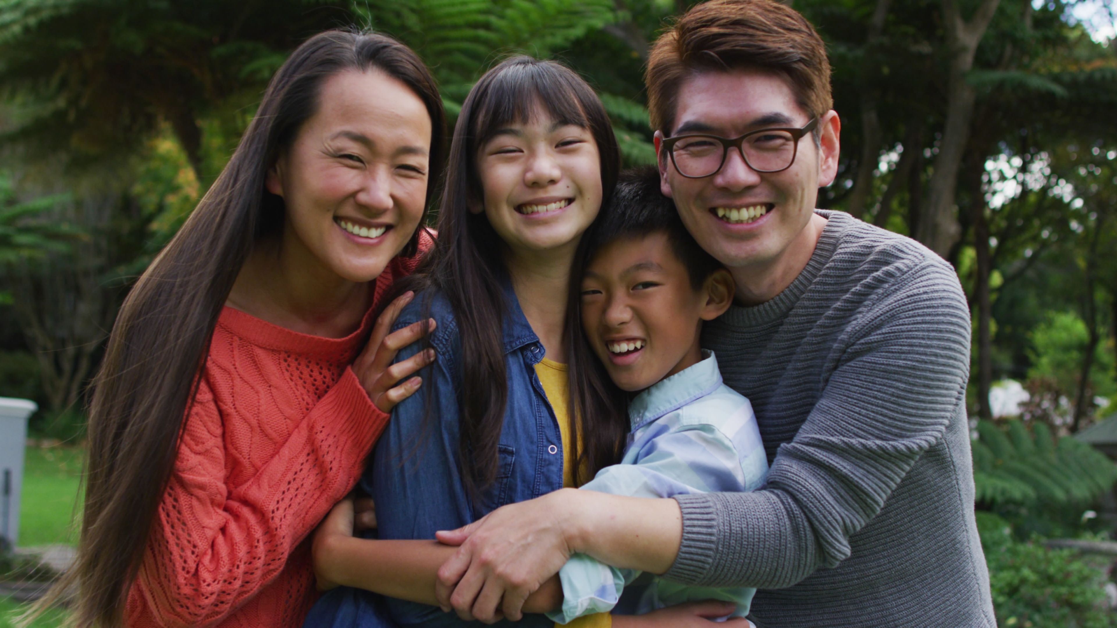 An Asian family of four smiles at the camera while hugging.