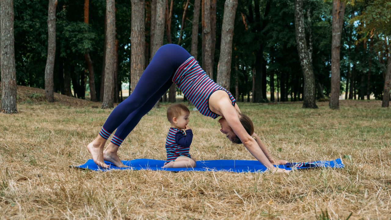 A mom does yoga on a mat on the grass with her baby on the mat with her