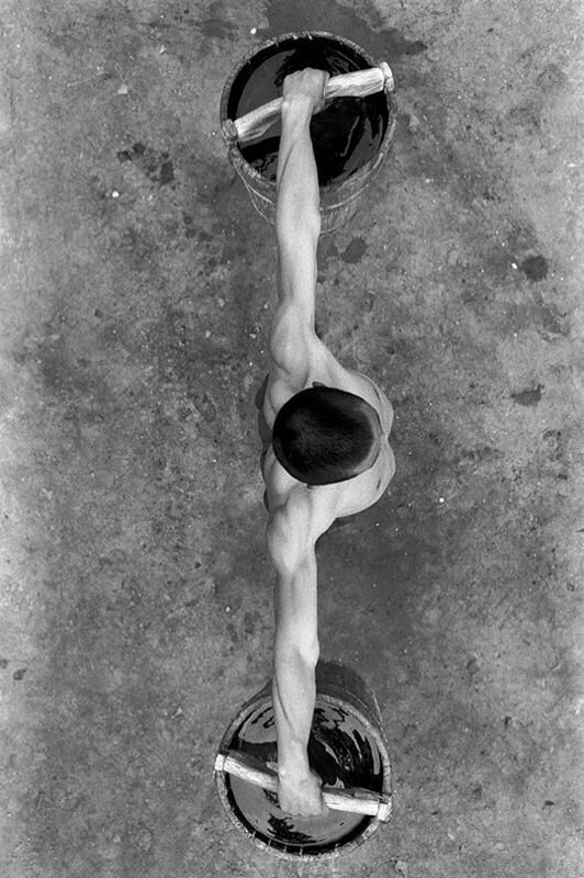 Man holding two buckets of water with arms extended