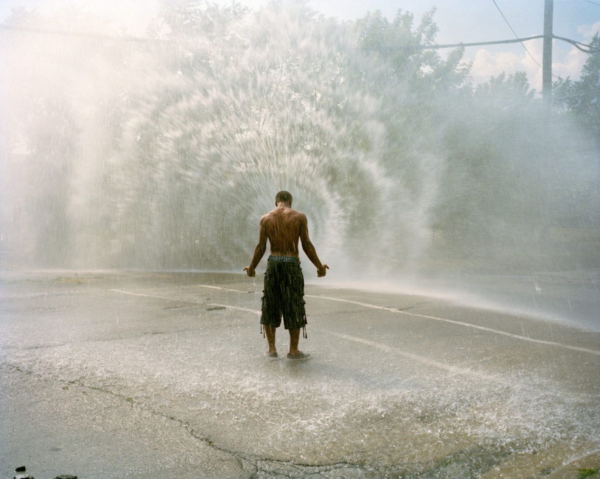 man standing peacefully in a street with water spraying up from a hidden source