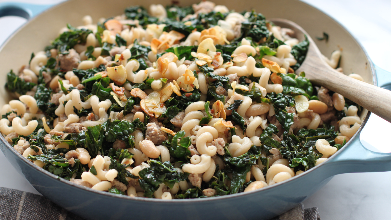 Gluten-free sausage, beans and greens pasta with kale, white beans, and crispy garlic in a skillet